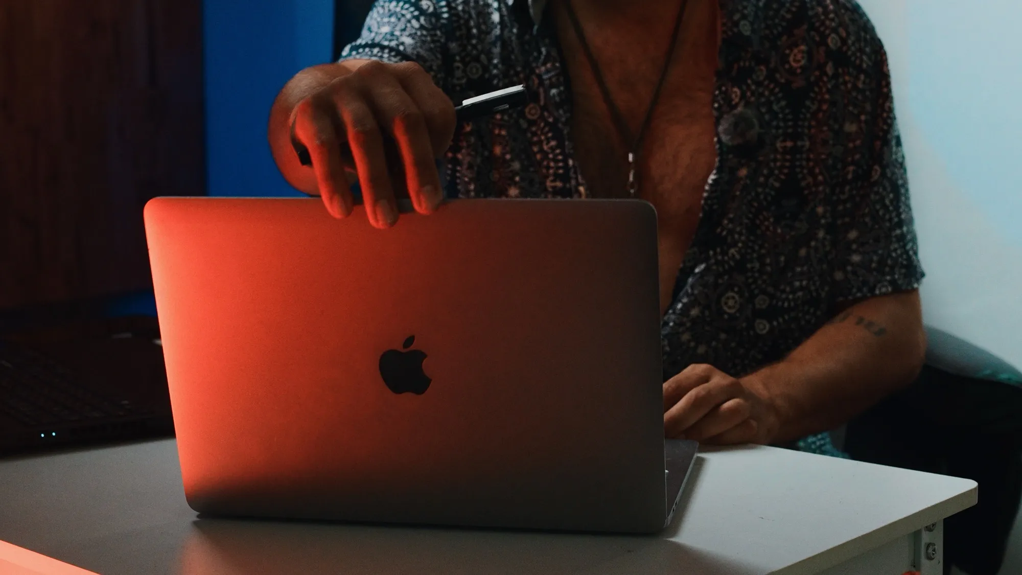 A hand holding a pen over a laptop lid lit in orange